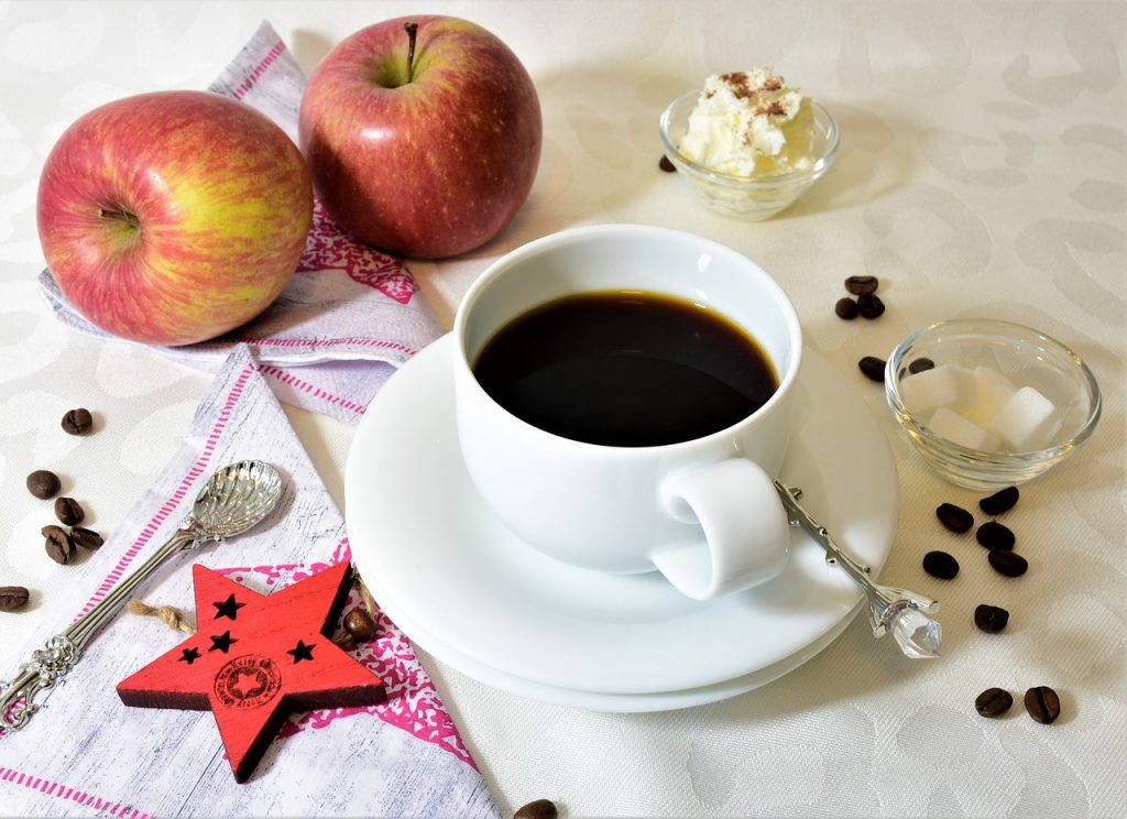 black coffee in white ceramic teacup with apples at side.